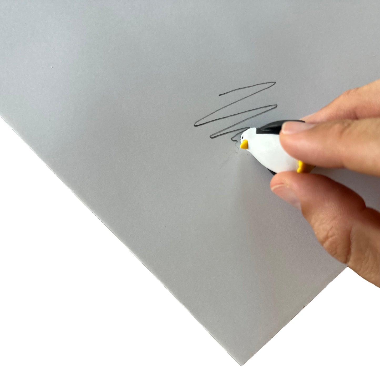 Hand using a penguin-shaped eraser to erase pencil from white paper
