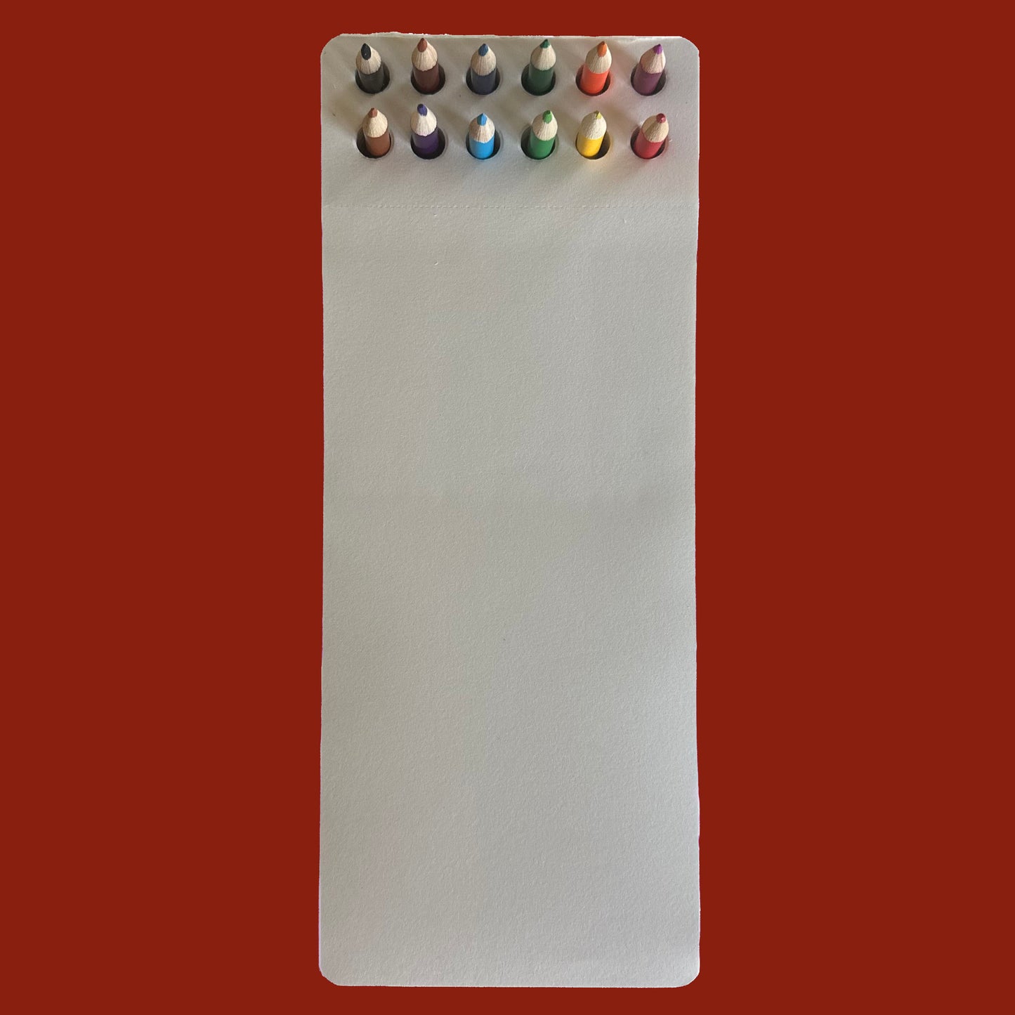 Set of colored pencils in a white notepad against a red background