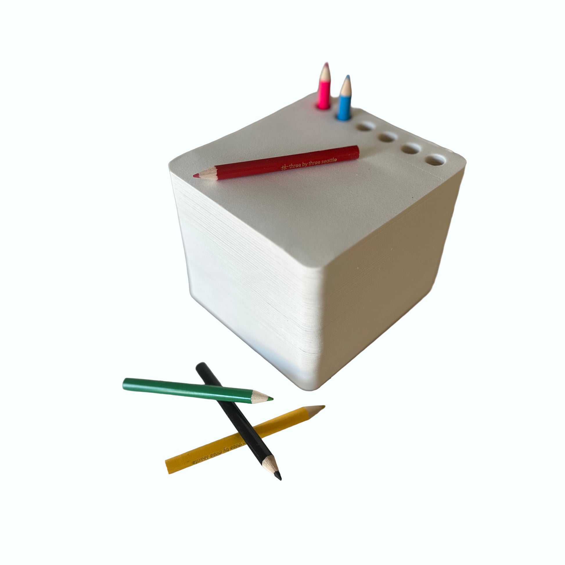 White rectangular sketchpad block with holes and colored pencils on a white background