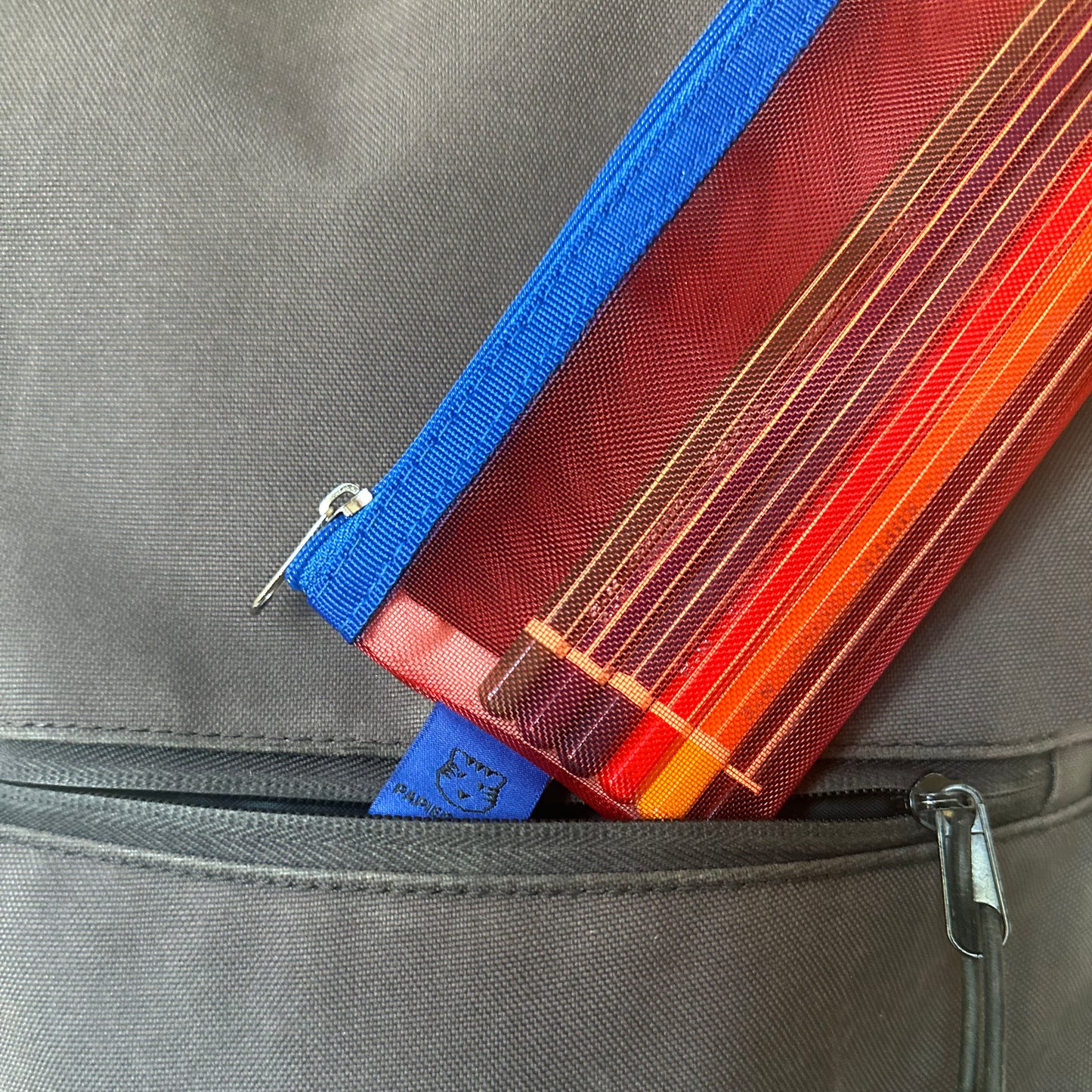 Red and blue pencil case being removed from black backpack