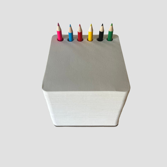 White sketchpad cube with colorful pencils inside on a white background